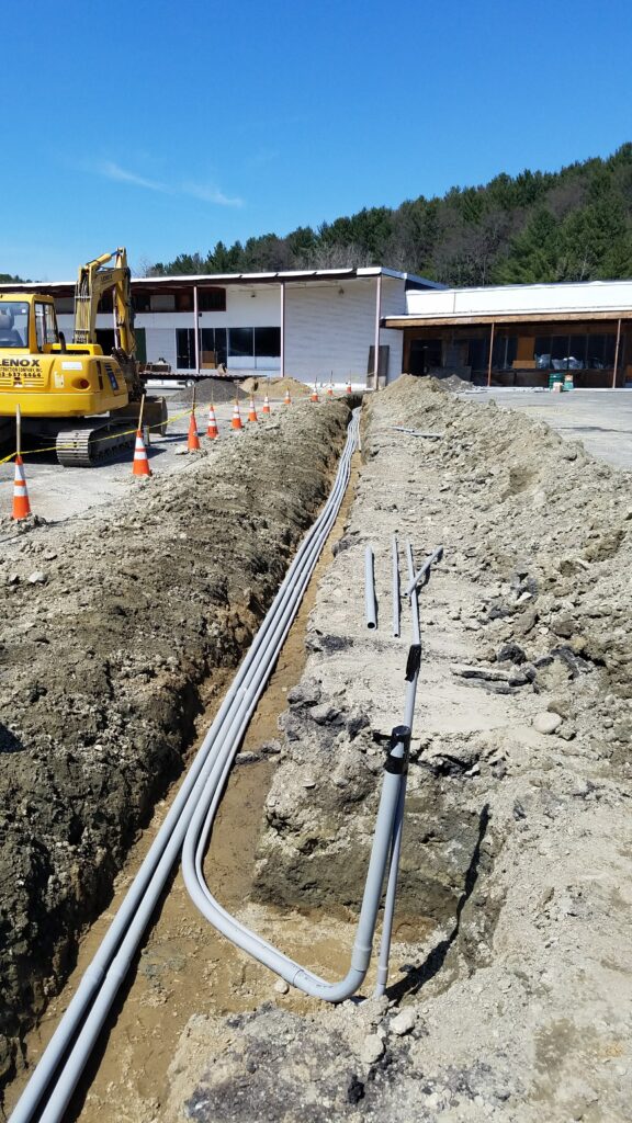 Underground electrical conduit trench installation for EV chargers and parking lot lighting by licensed electricians in Connecticut and Massachusetts.